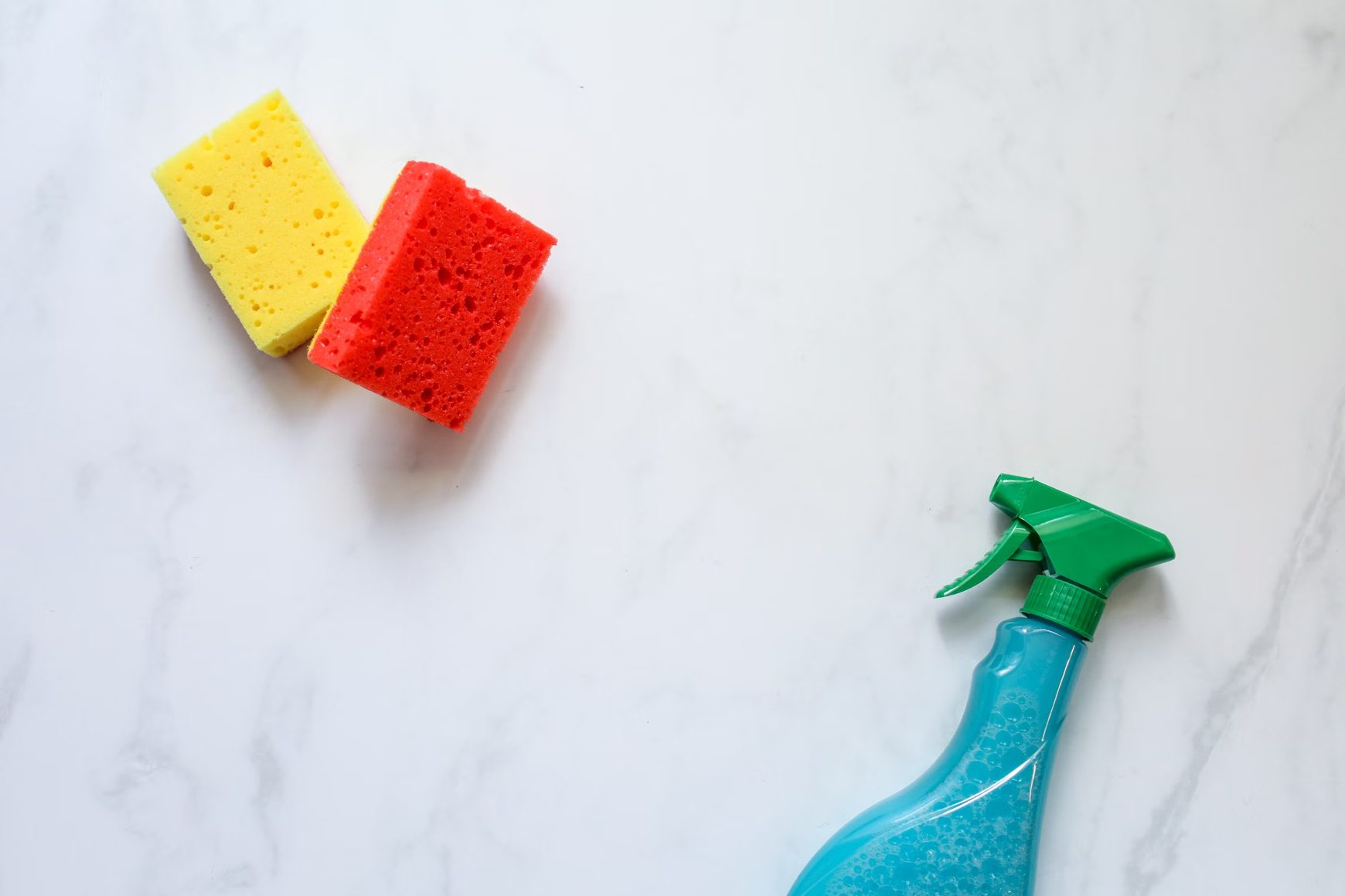 Red and yellow cleaning sponges beside a plain blue spray bottle.