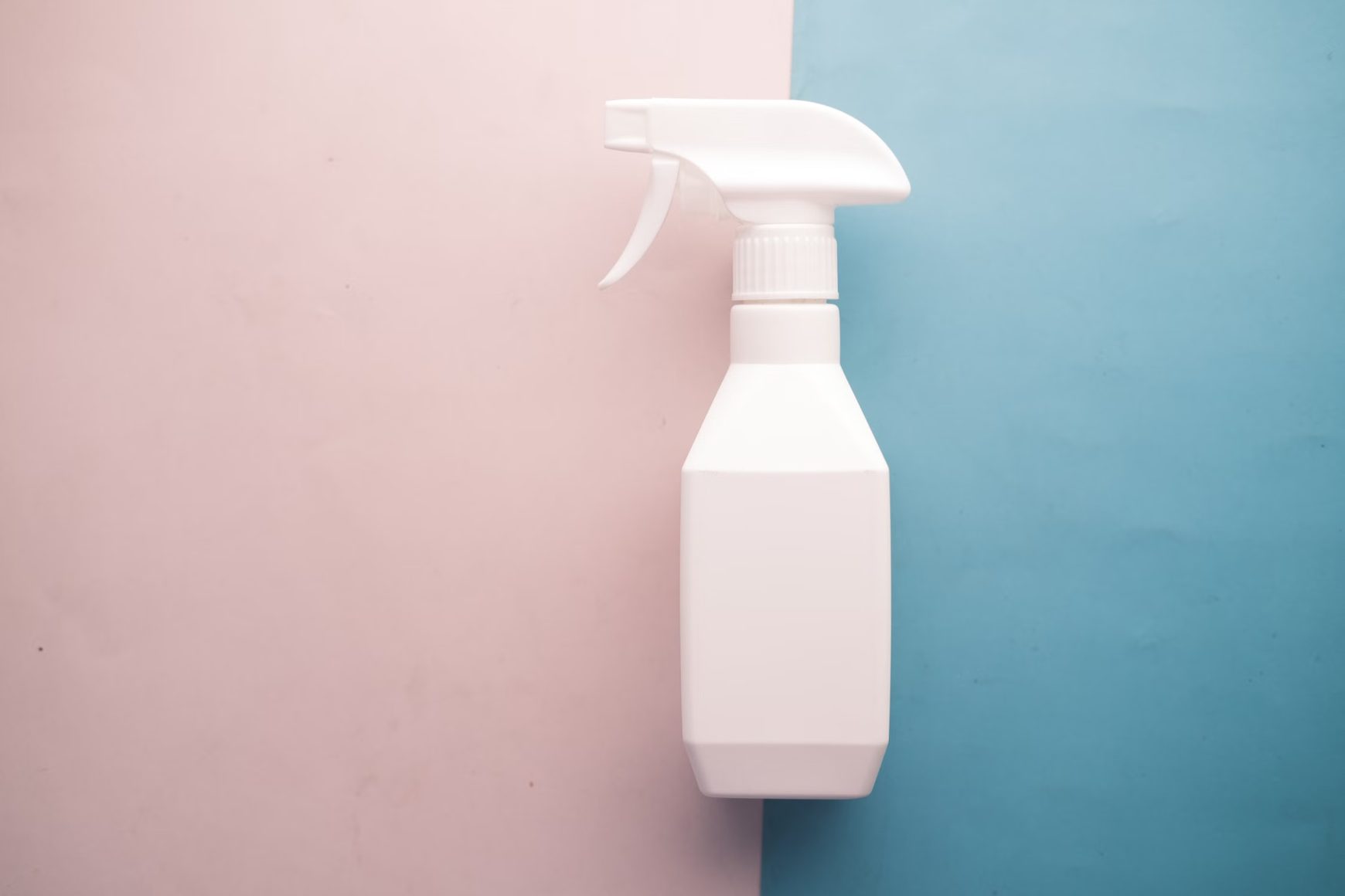 Plain white spray bottle on a blue and pink background.