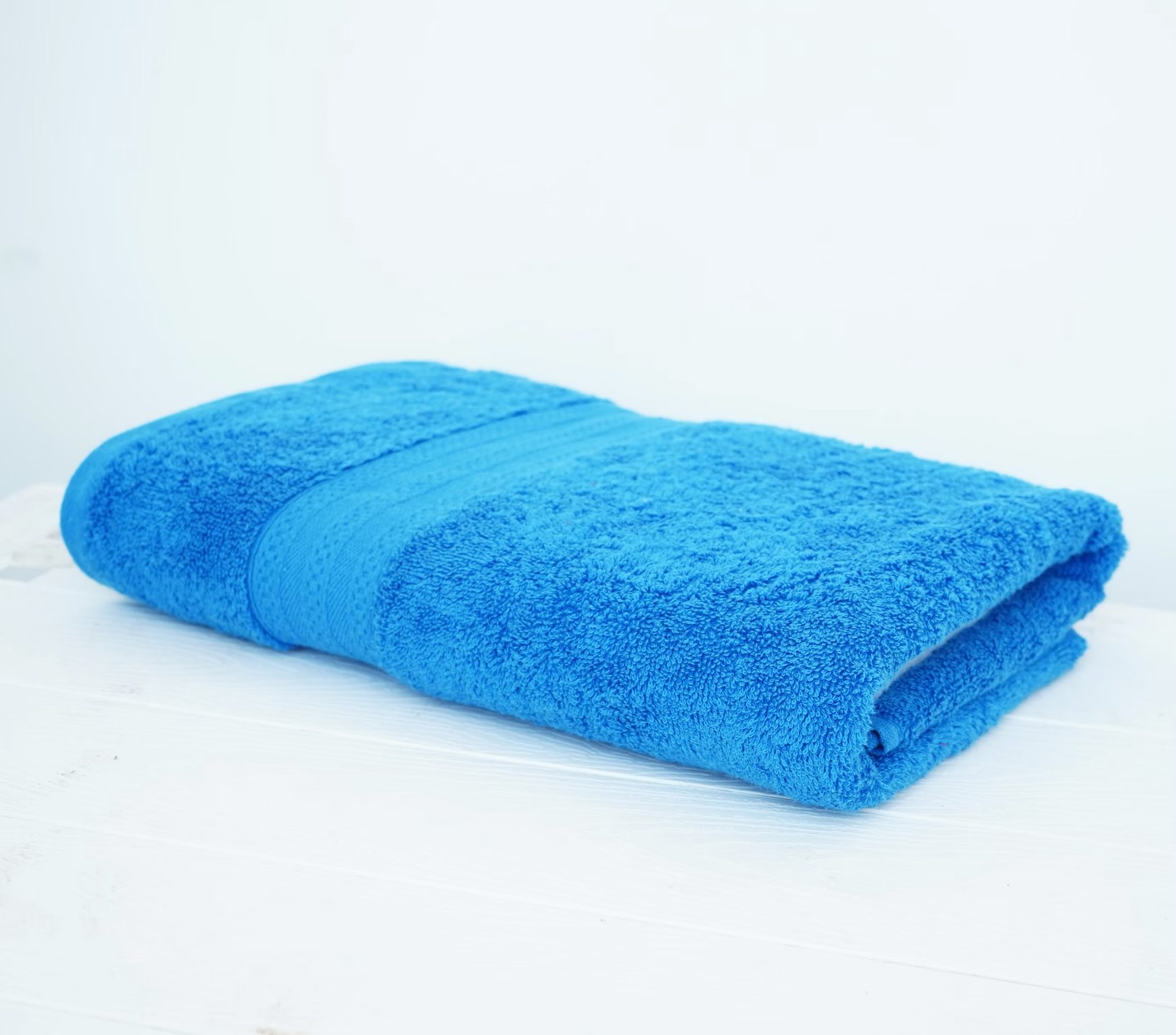 A plain blue towel folded on a white surface