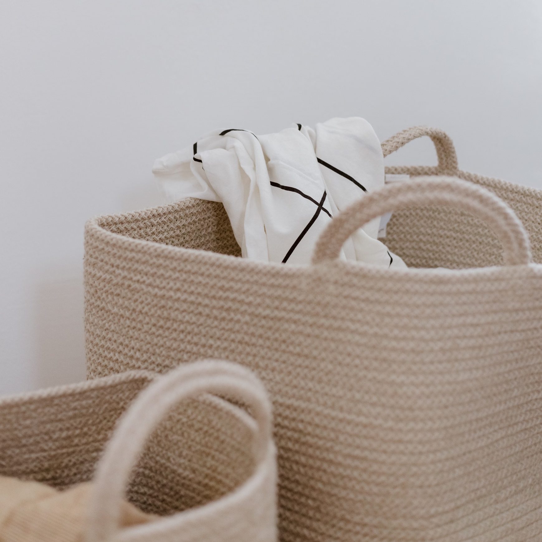 Neutral woven laundry baskets holding white linen with narrow dark woven lines.