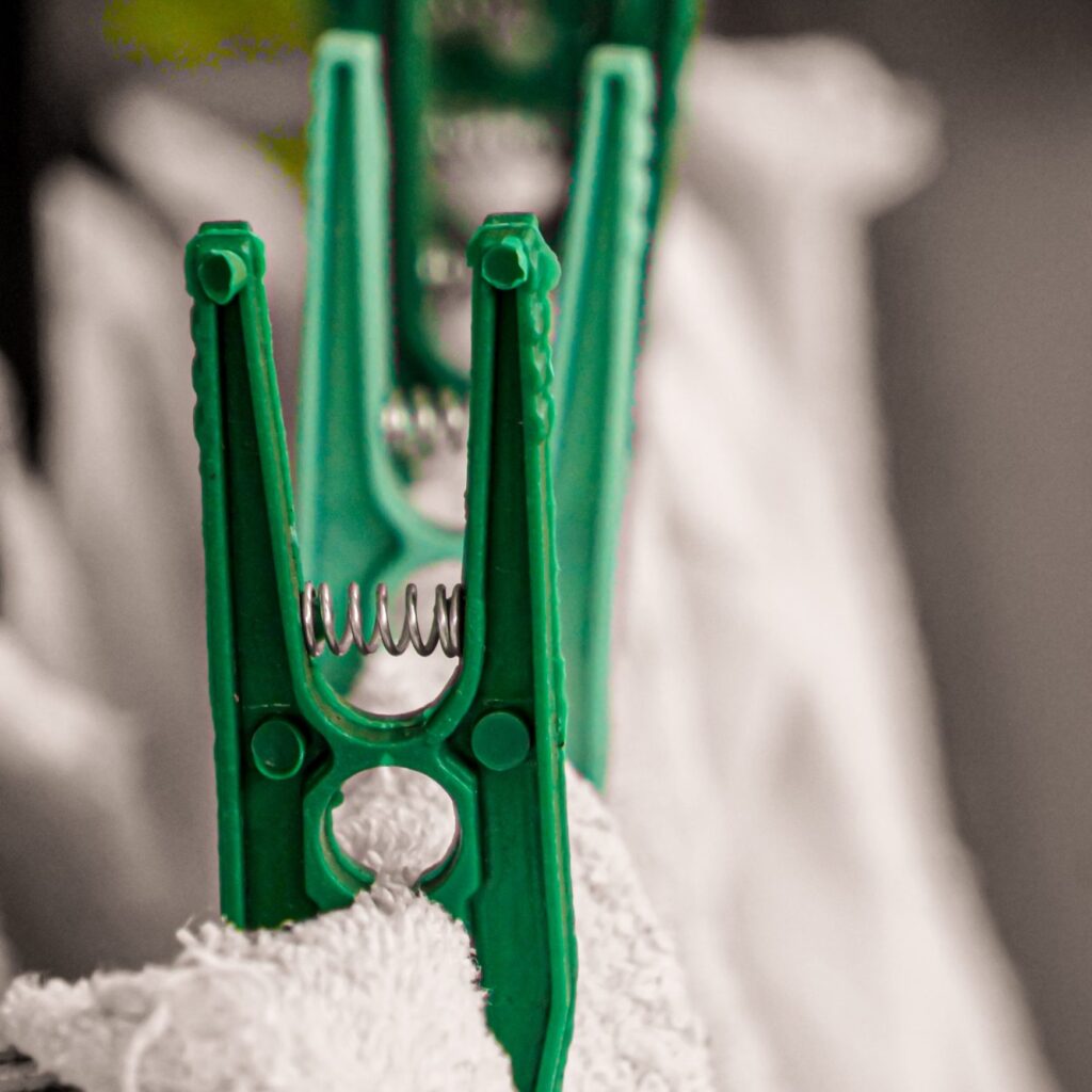 Green spring pegs holding a white towel on a drying line.