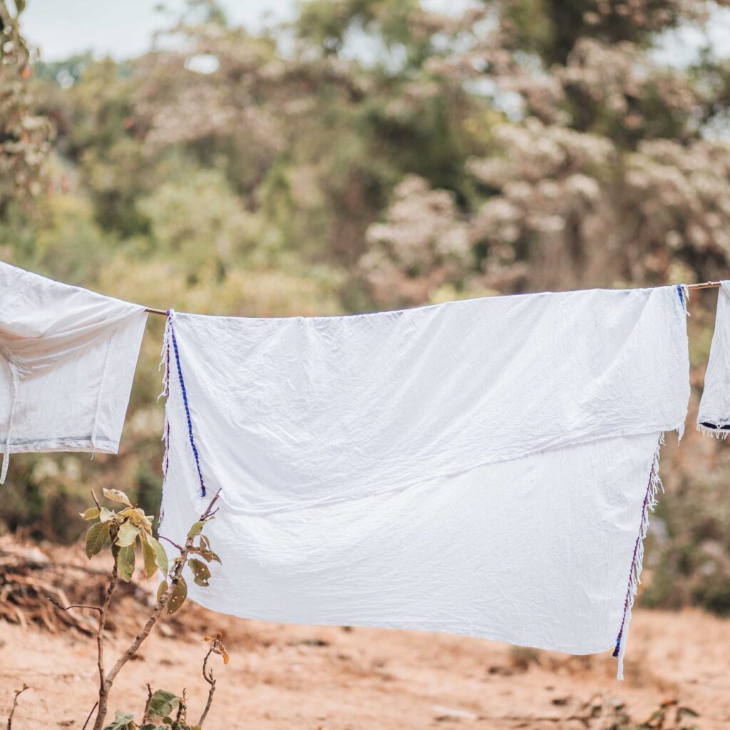 White linen with narrow blue woven edges hanging on an outdoor line among trees.