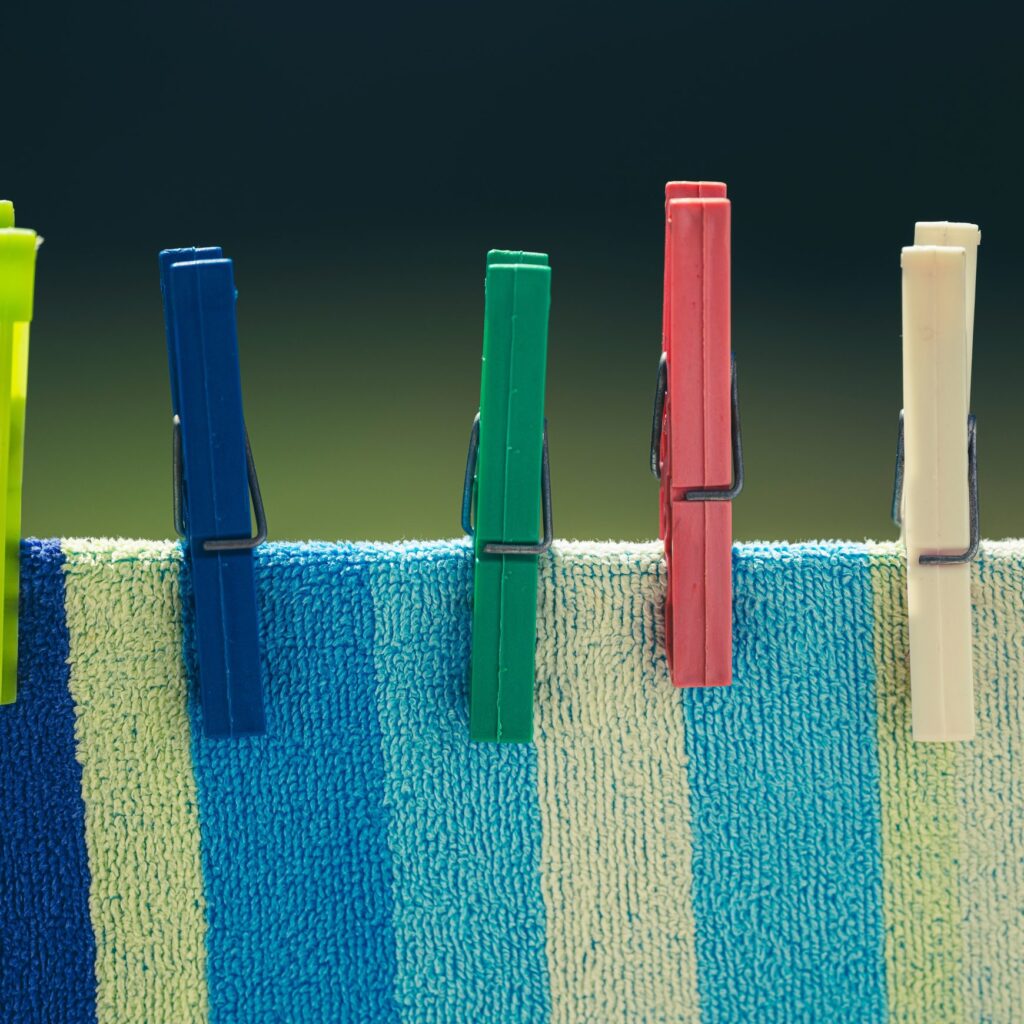 Colourful clothes pegs securing a blue and cream striped towel on a drying line.