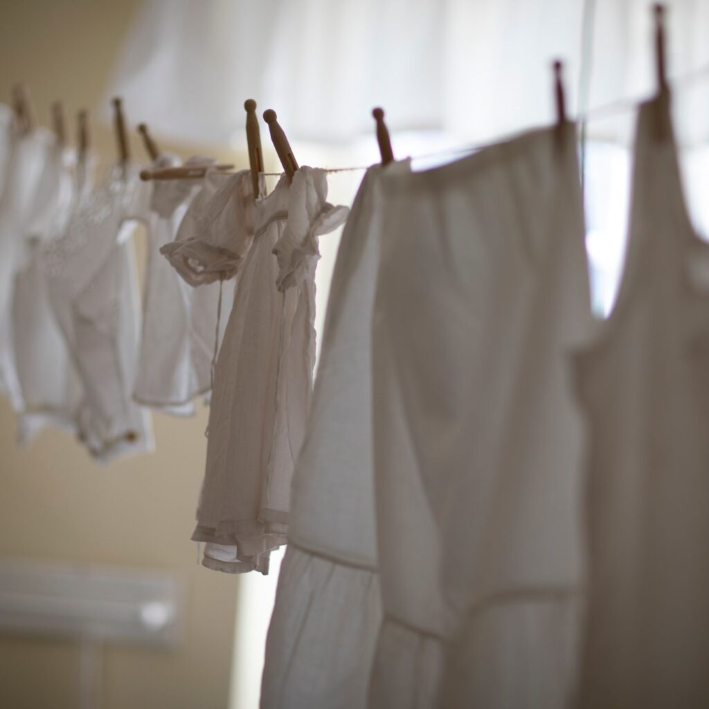 Plain white garments drying on a line with wooden pegs in soft window light.