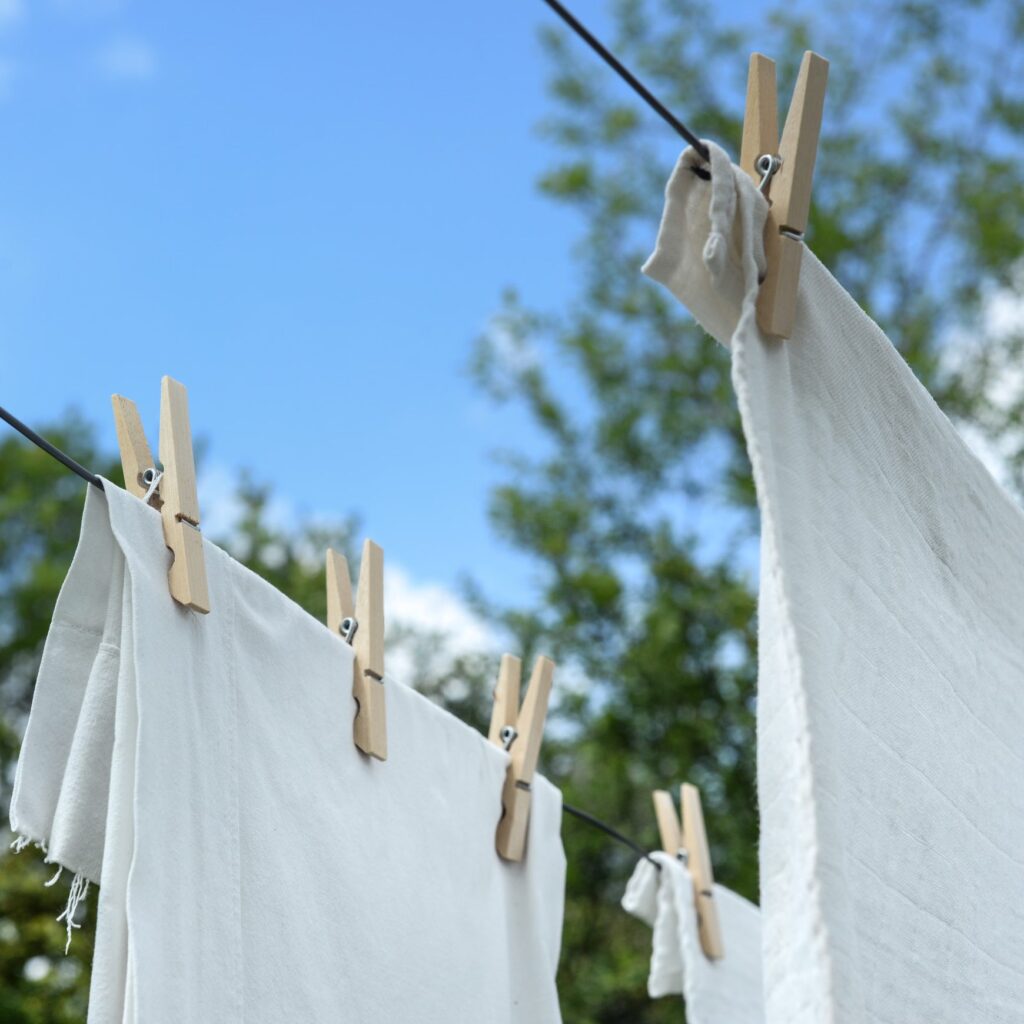 White fabric secured by wooden clothes pegs on outdoor lines against trees and blue sky.