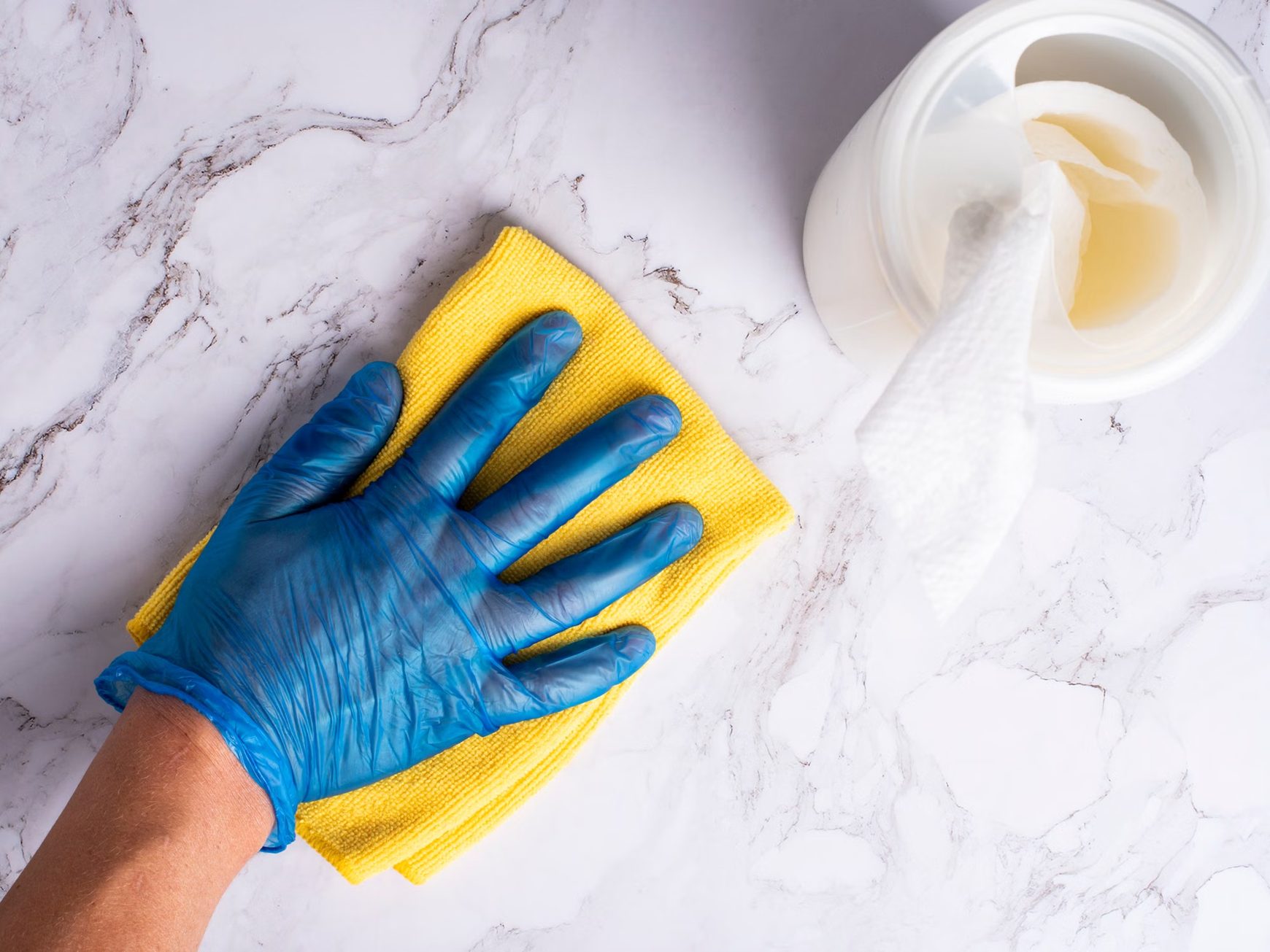 Blue-gloved hand wiping a marble-pattern countertop with a yellow microfibre cloth.