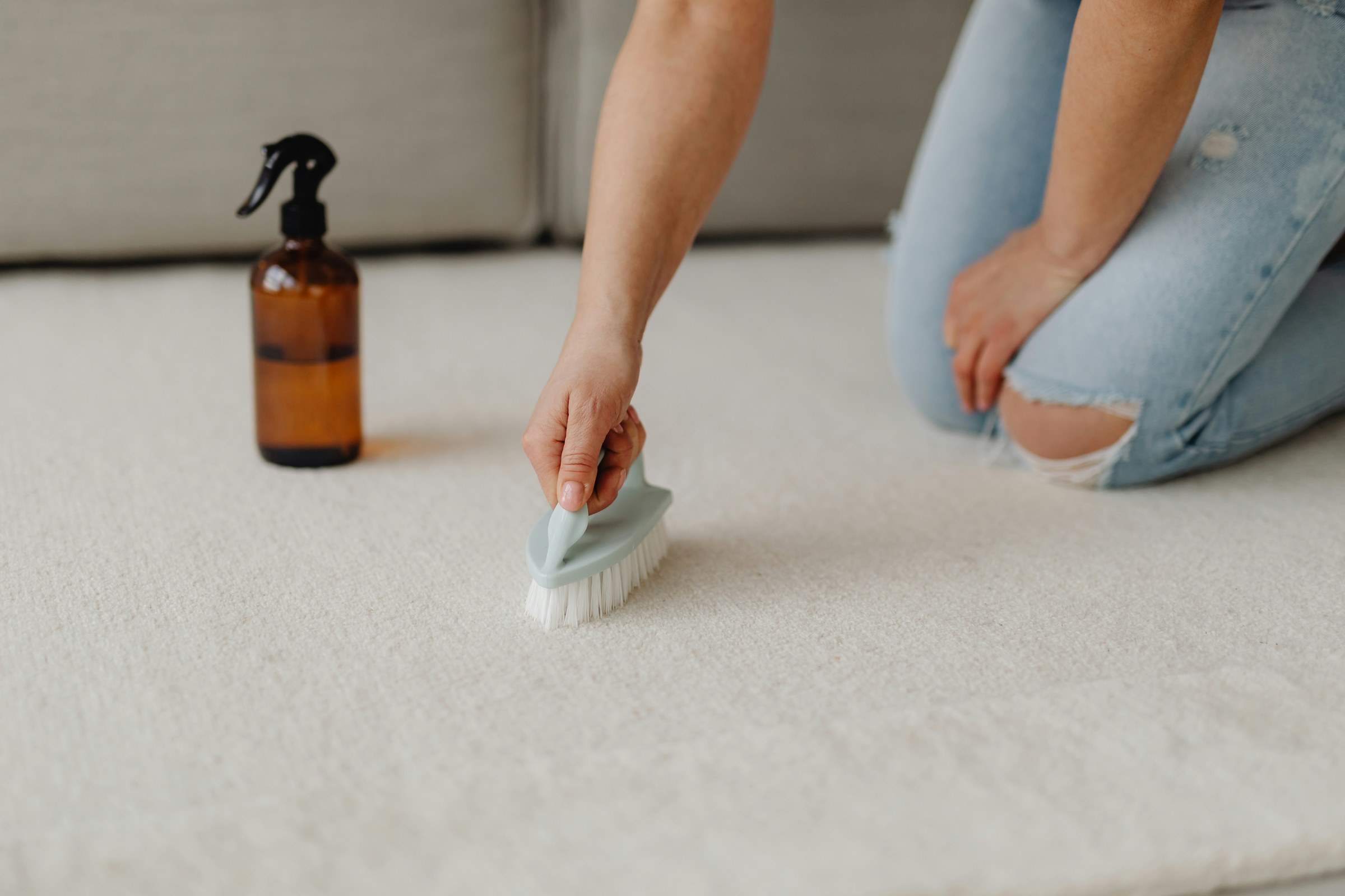 Person using a hand brush on a light-coloured carpet.