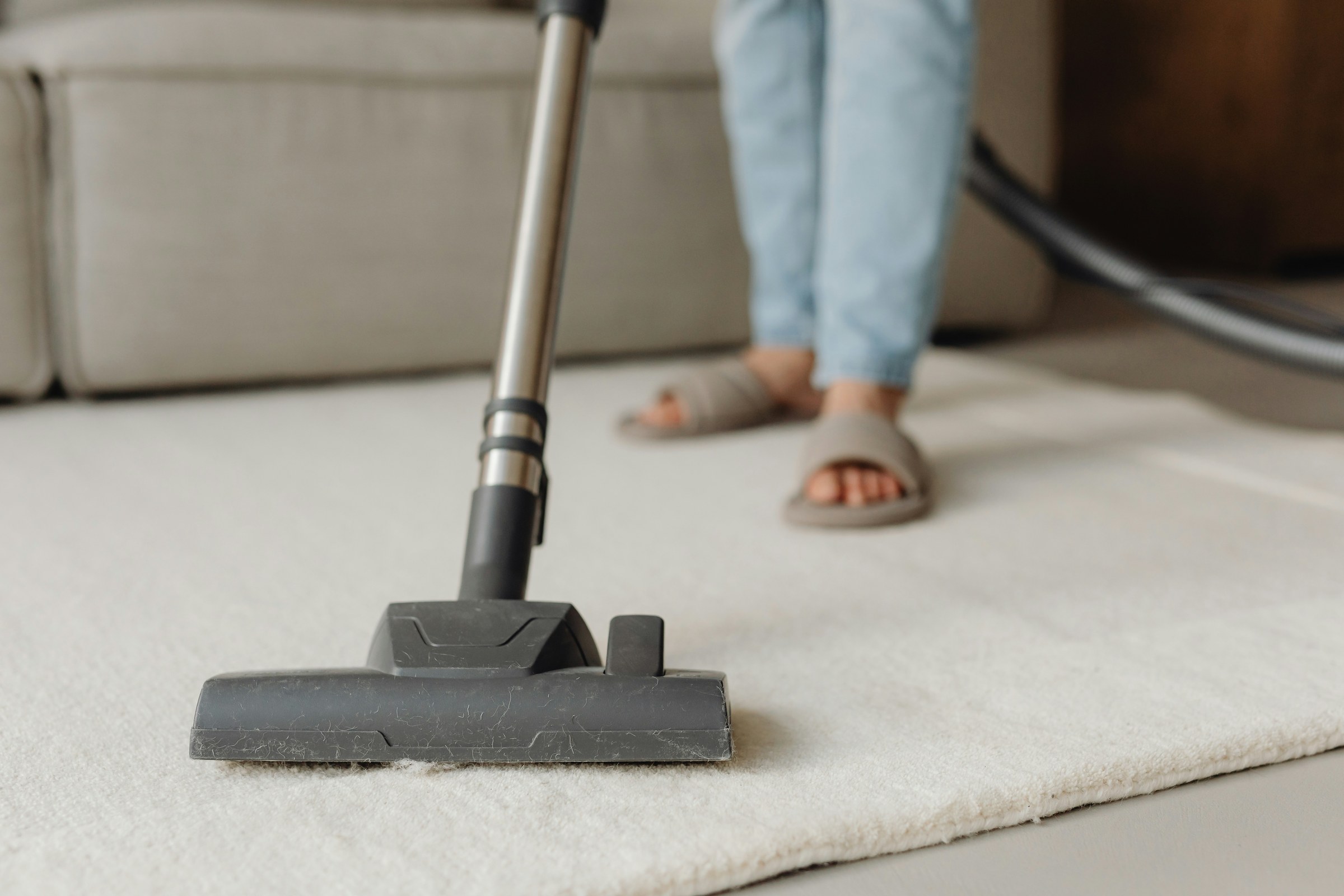 Person vacuuming a light-coloured rug.